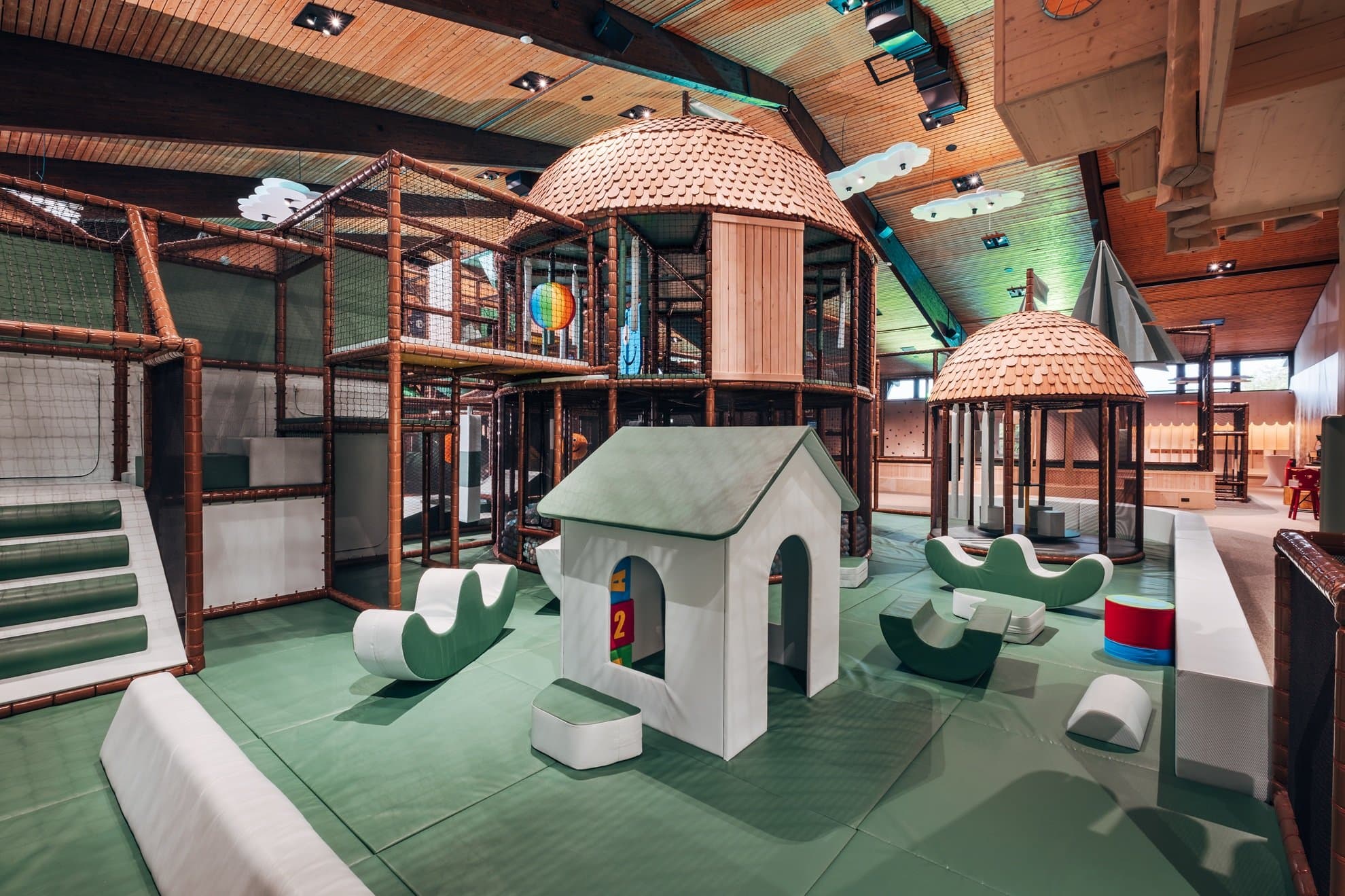 Kleinkinder-Erlebnisbereich mit kleinem Haus und verschiedenen Kletterelementen darum angeordnet. Dahinter Kletterhaus mit verschiedenen Ausbauten über 2 Etagen.