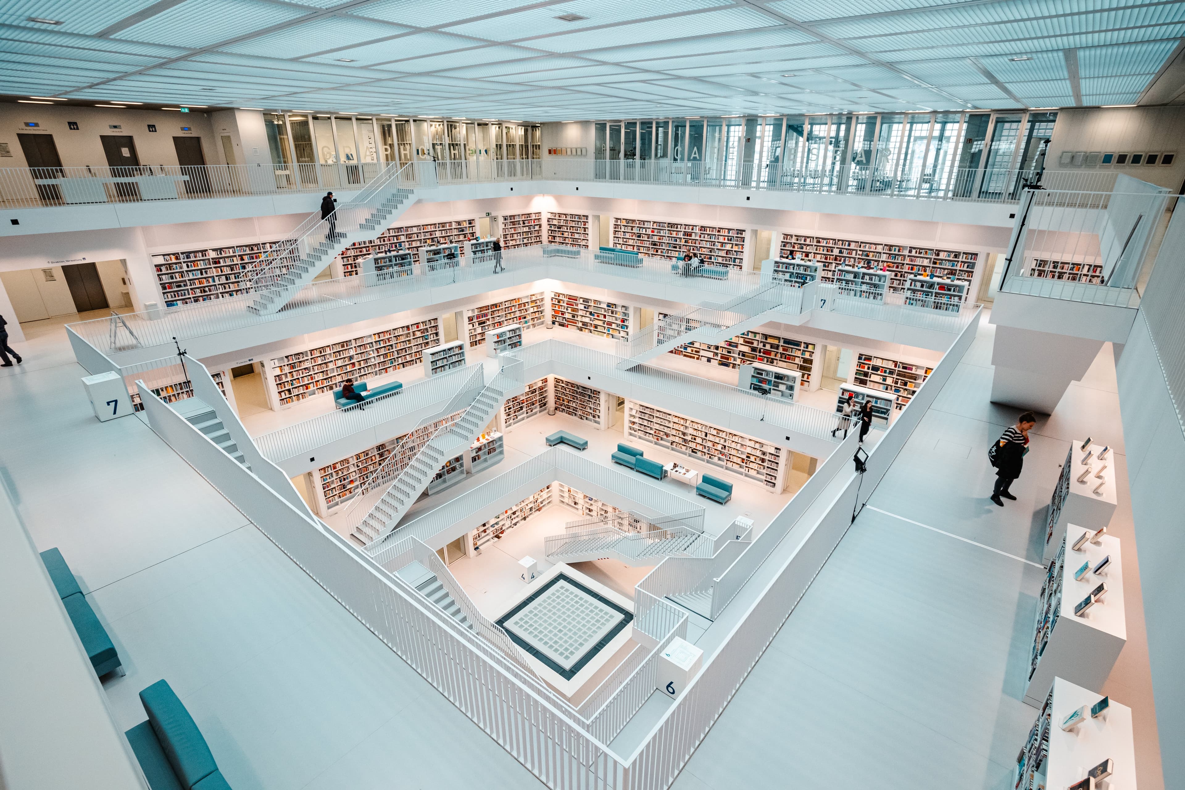 Innenansicht einer modernen, mehrstöckigen Bibliothek mit weißen Wänden und Regalen voller Bücher.