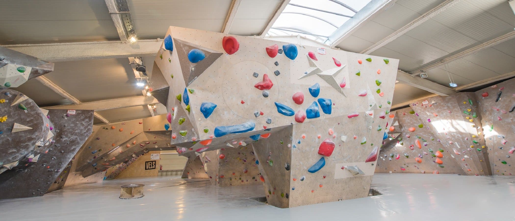 Innenansicht einer Boulderhalle mit verschiedenen Kletterwänden und bunten Griffen.