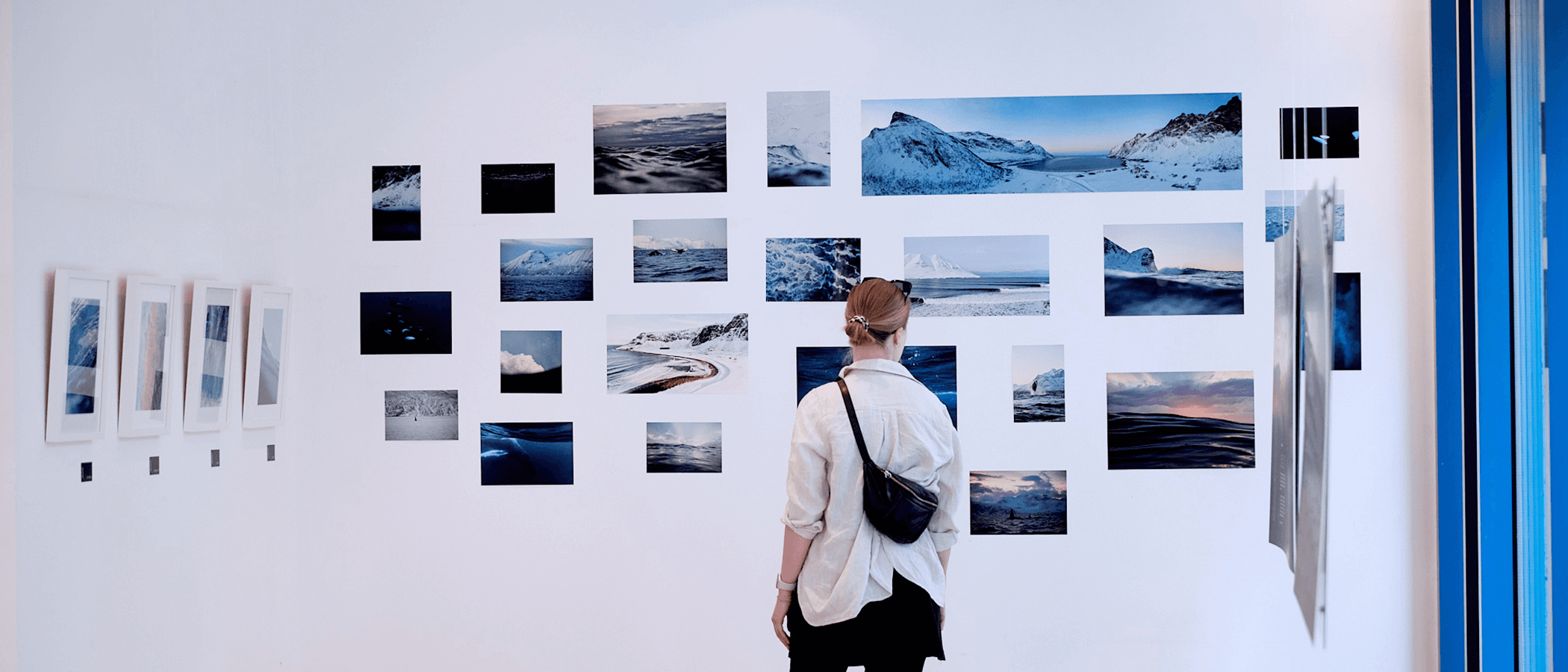 Person betrachtet eine Wand mit Fotografien von Landschaften und Wasser.