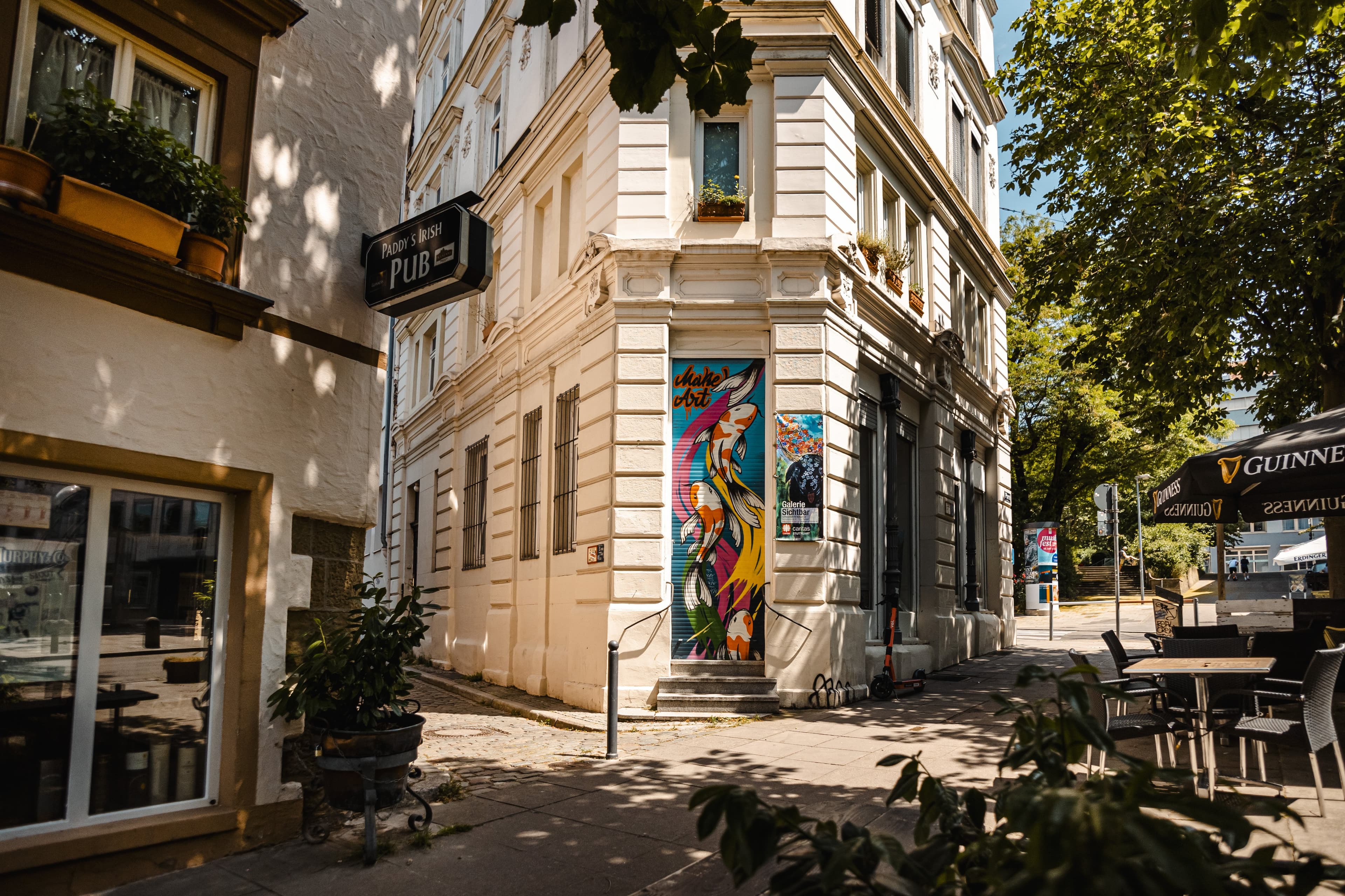 Straßenszene mit Pub-Schild, Wandkunst und Café-Tischen.