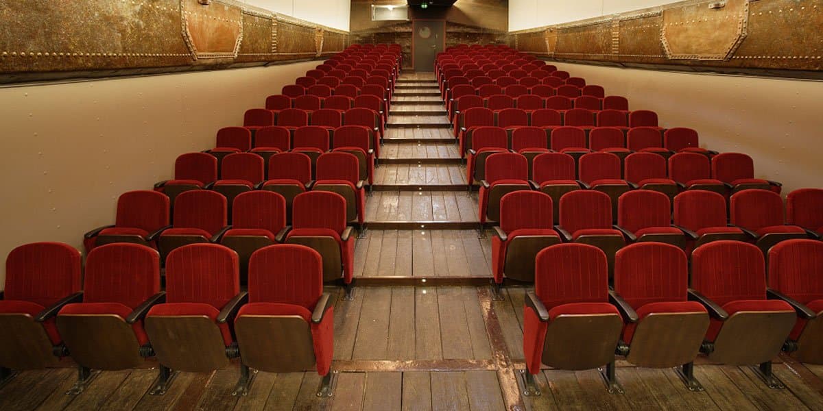 Innenansicht eines Theatersaals mit roten Sitzreihen auf einem Schiff.