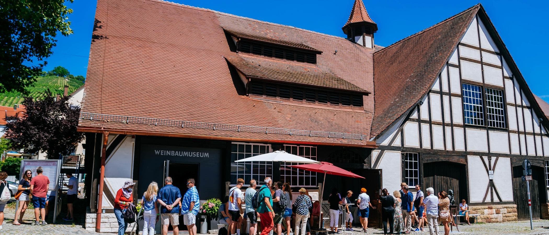 Menschen vor dem Weinbaumuseum in Uhlbach bei sonnigem Wetter.