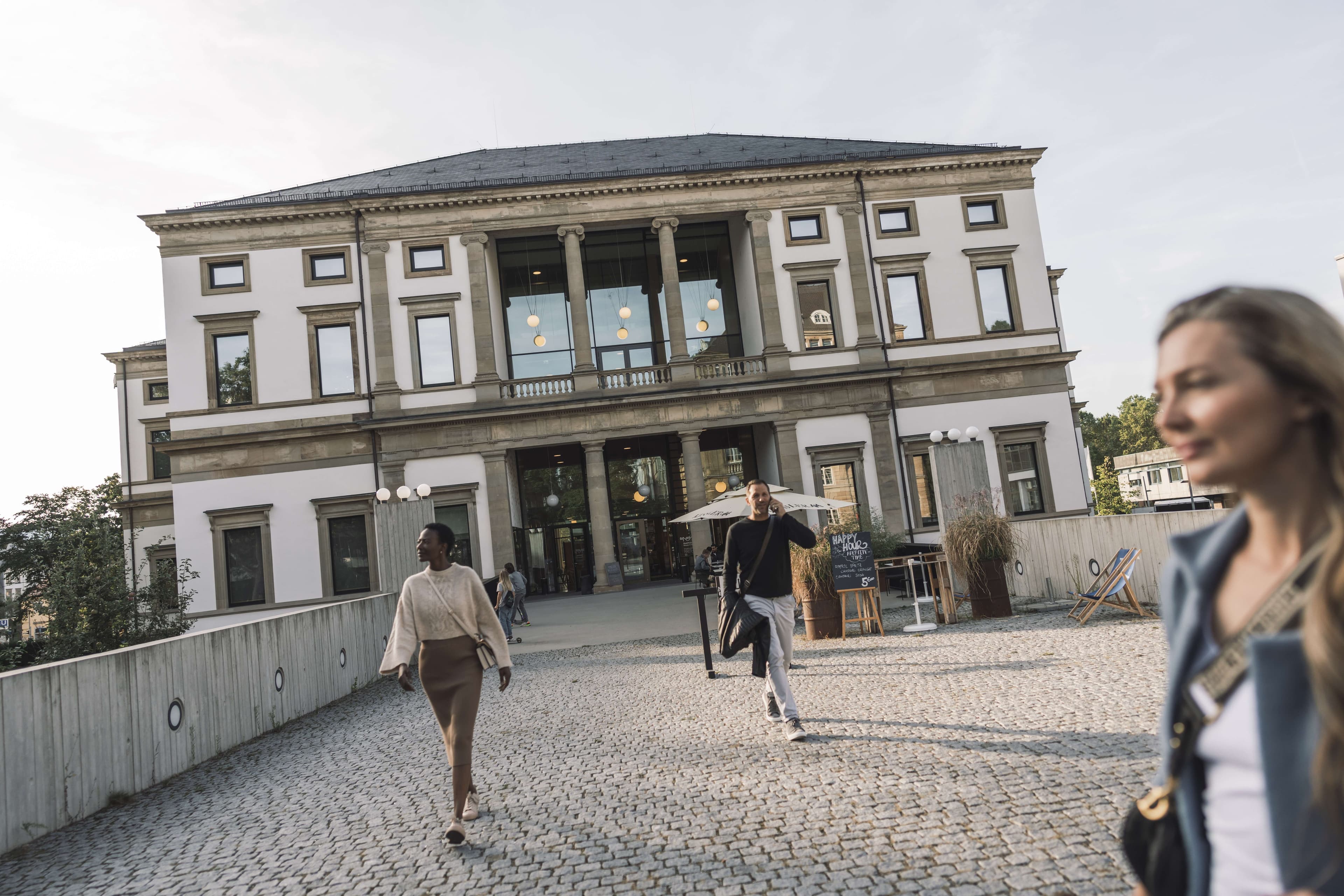 Menschen gehen vor dem StadtPalais Stuttgart auf einem gepflasterten Weg.