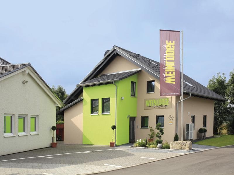 Building seen from the outside with green and brown colours and a large flag in the foreground with wine lodge