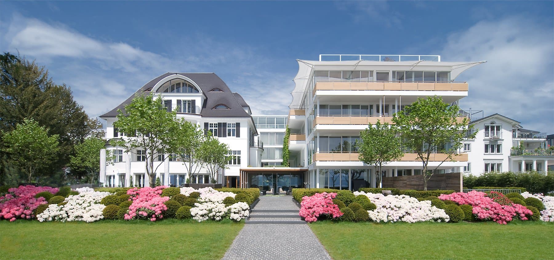 Das Hotel RIVA - eine elegante Jugendstilvilla neben dem lichtdurchfluteten Neubau. Im Vordergrund sind Blumenbeet zu sehen.