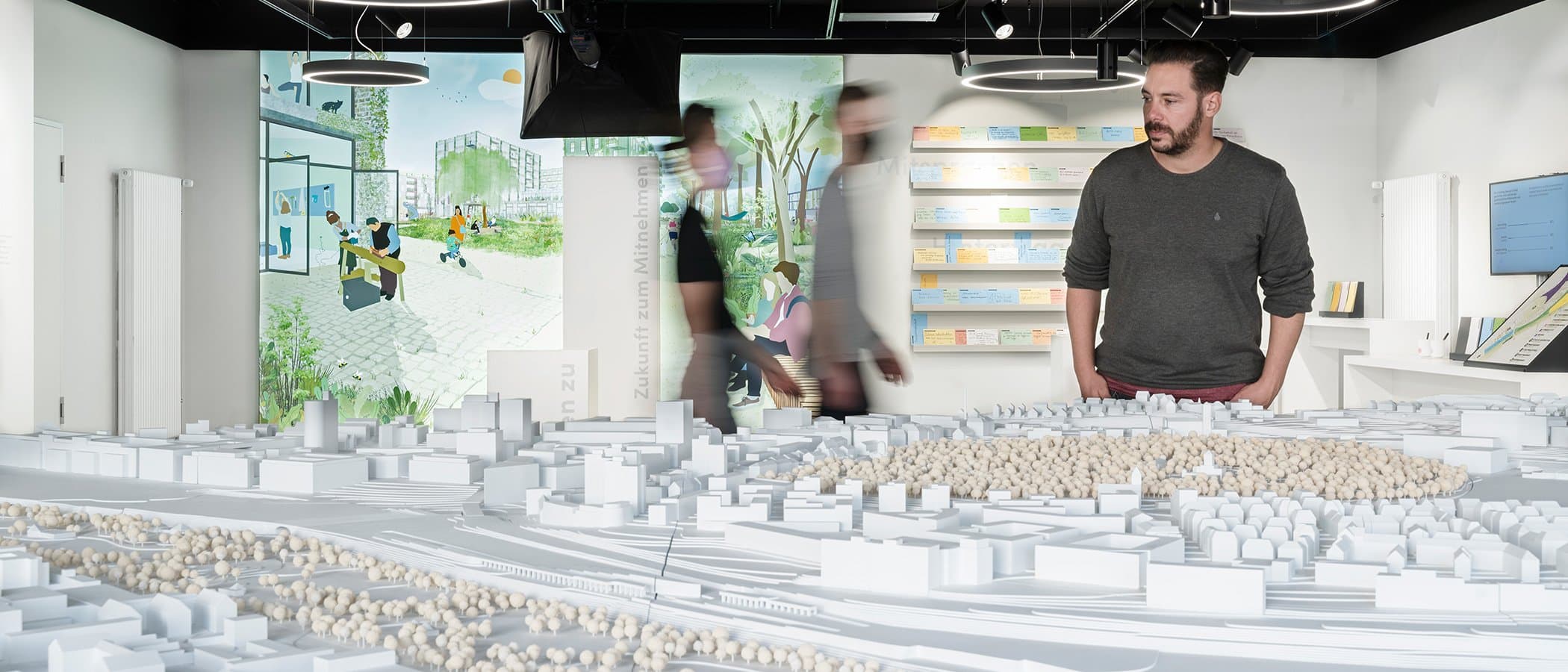 Ein Mann betrachtet ein Architekturmodell in einer Ausstellung mit Illustrationen im Hintergrund.