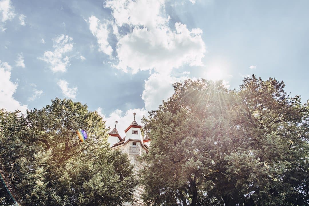 A tower with pointed roofs and a flag, surrounded by trees and sunbeams.