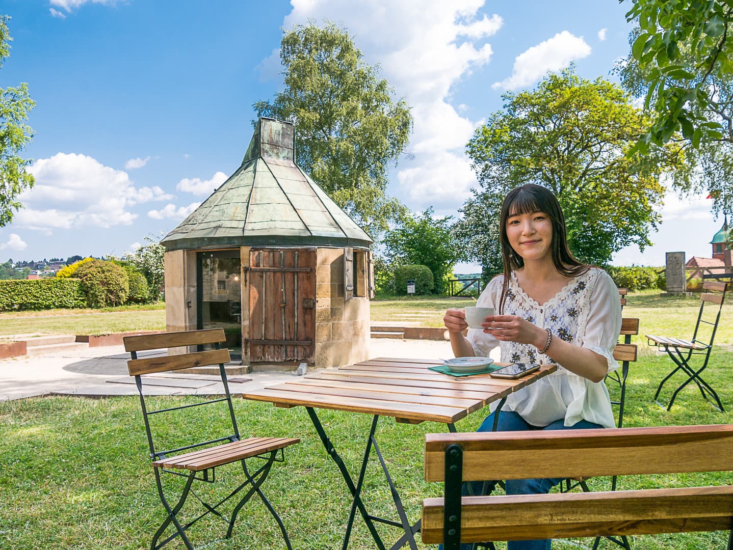 Junge, japanische Studentin sitzt vor der Schloss-Sternwarte und trinkt eine Tasse Kaffee.