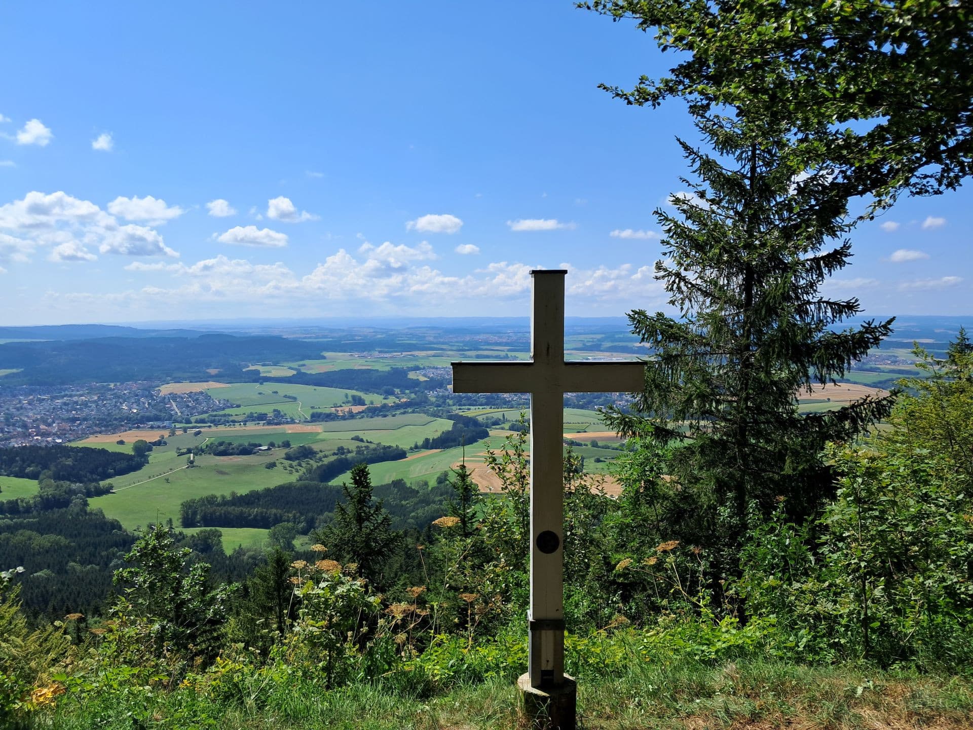 Aussicht vom Albtrauf in die weite Landschaft, im Vordergrund ein Gipfelkreuz