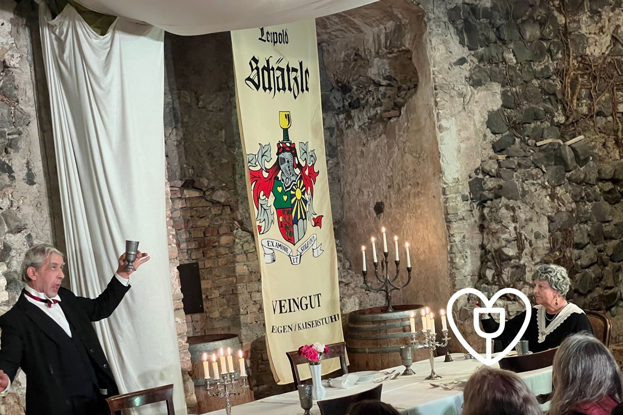 Zwei Schauspieler bringen Dinner for One auf die Bühne und prosten sich in der Szene zu