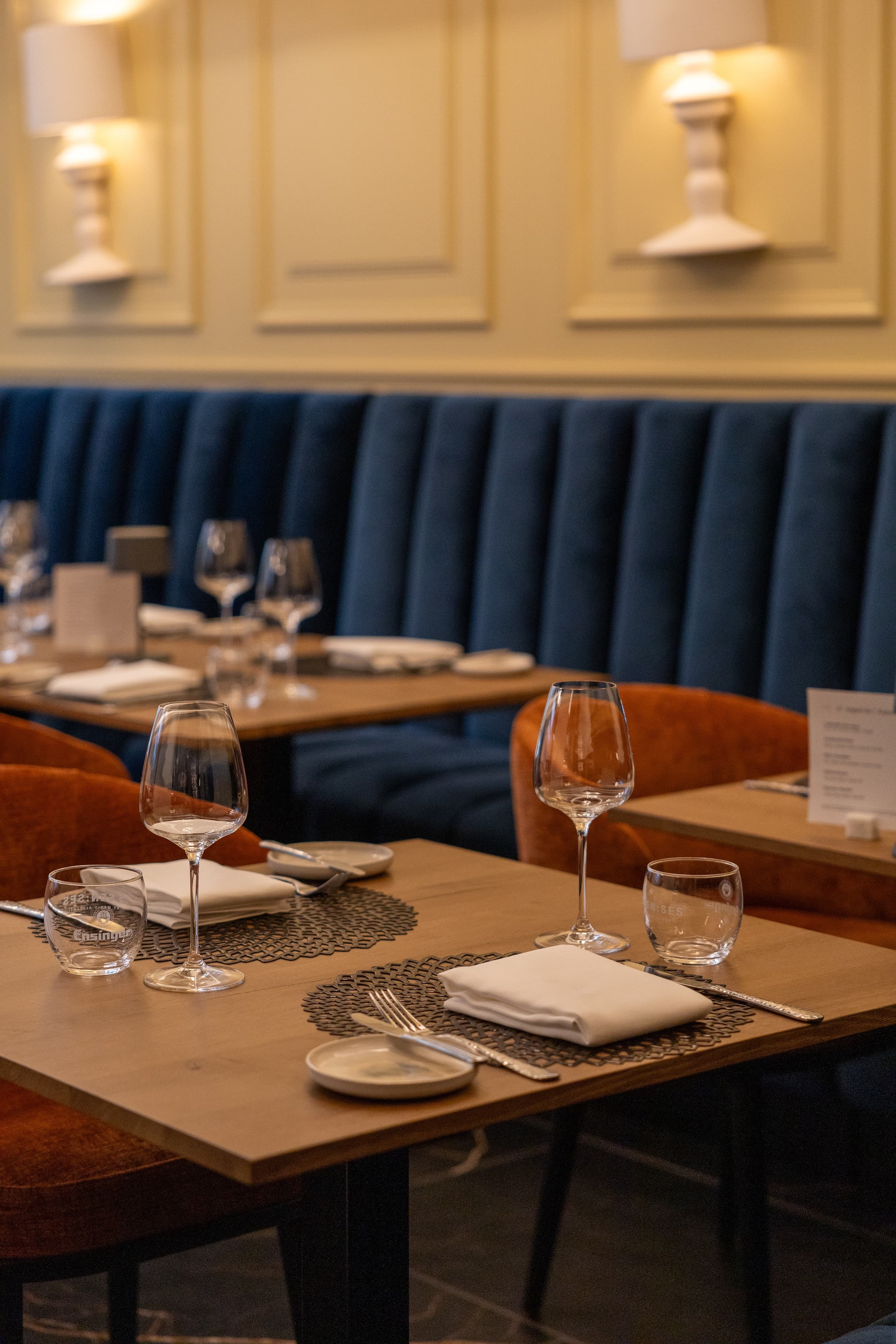 Im HIntergrund blaue Samtbank davor gedeckte Tische mit orangenen Samtstühlen