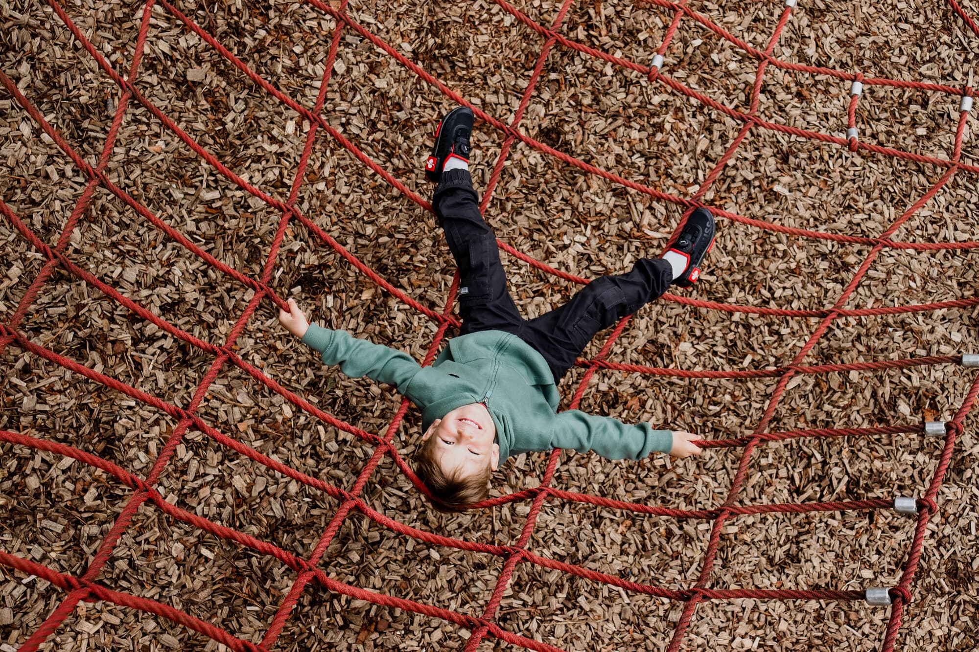 Auf dem Bild sieht man ein Jungen, welcher auf einem roten Seilnetz des Kletterparkours im Park der Zeiten liegt.