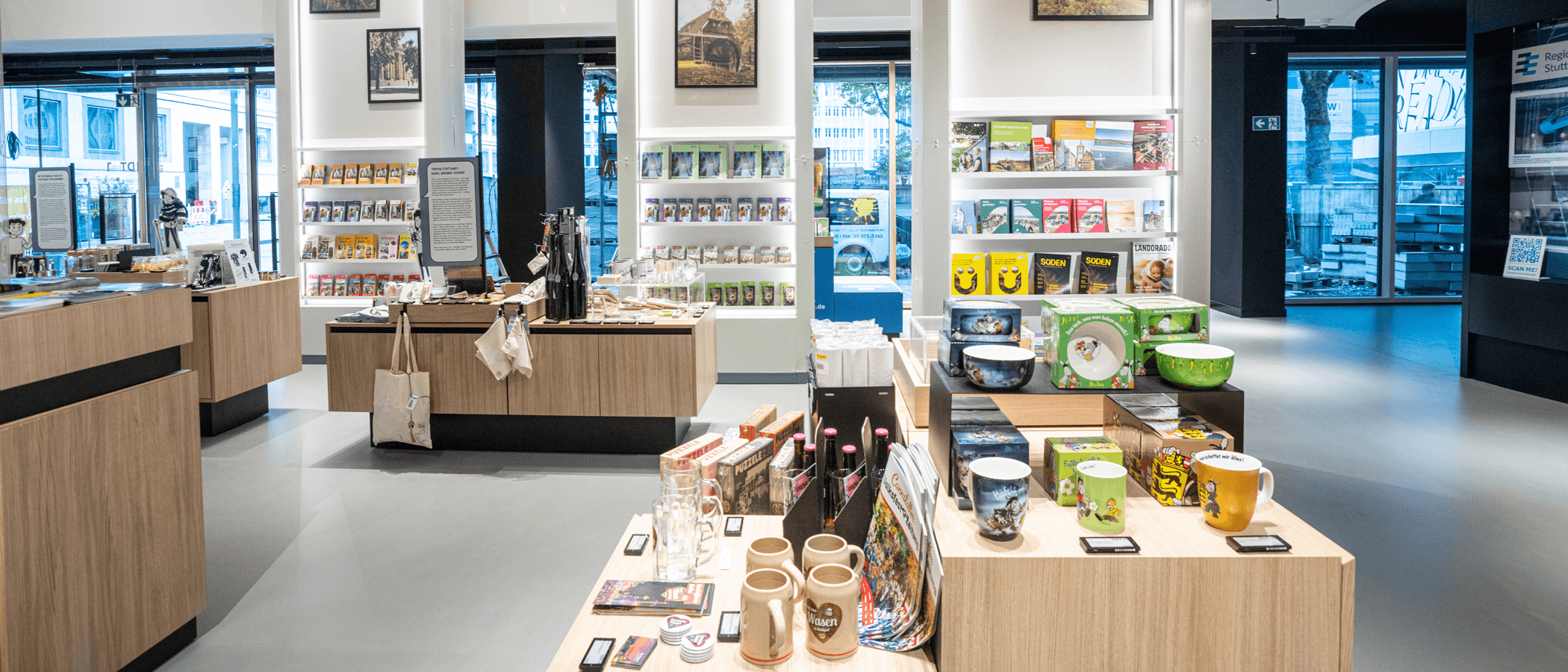 Interior view of a modern souvenir shop with shelves full of books, mugs and regional products.