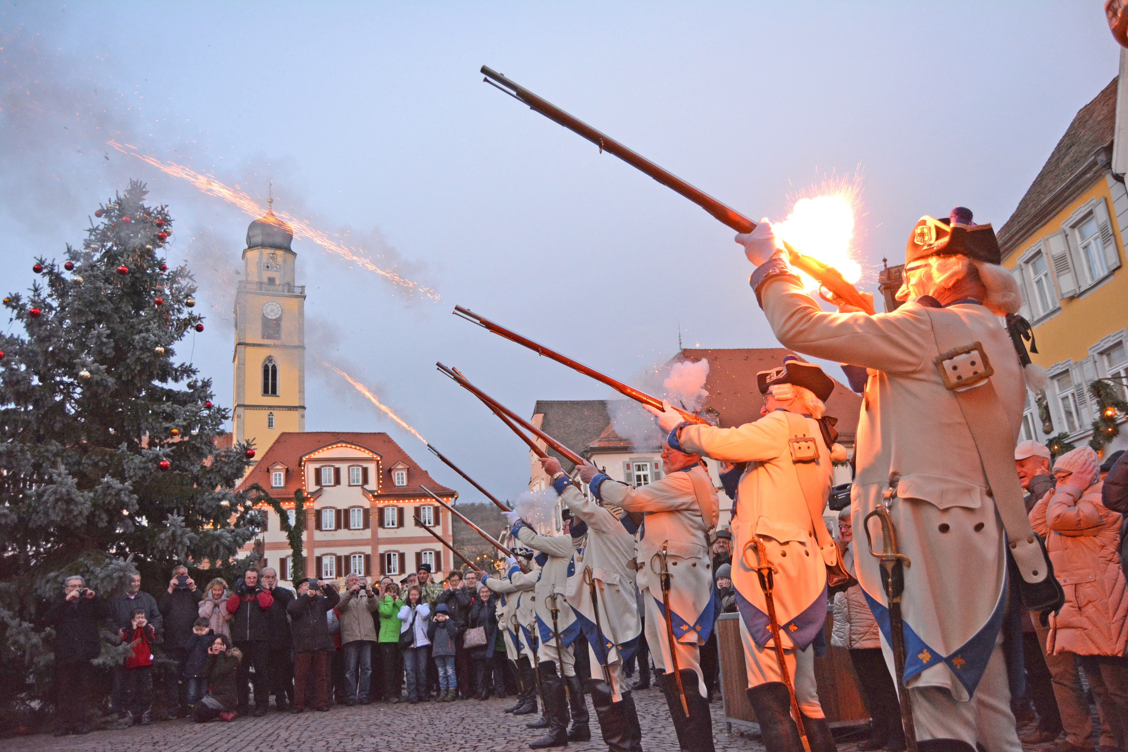 Die Historische Deutschorden Compagnie schießt auf dem Marktplatz mit ihren Gewähren in die Luft. Zuschauer schauen begeistert zu.