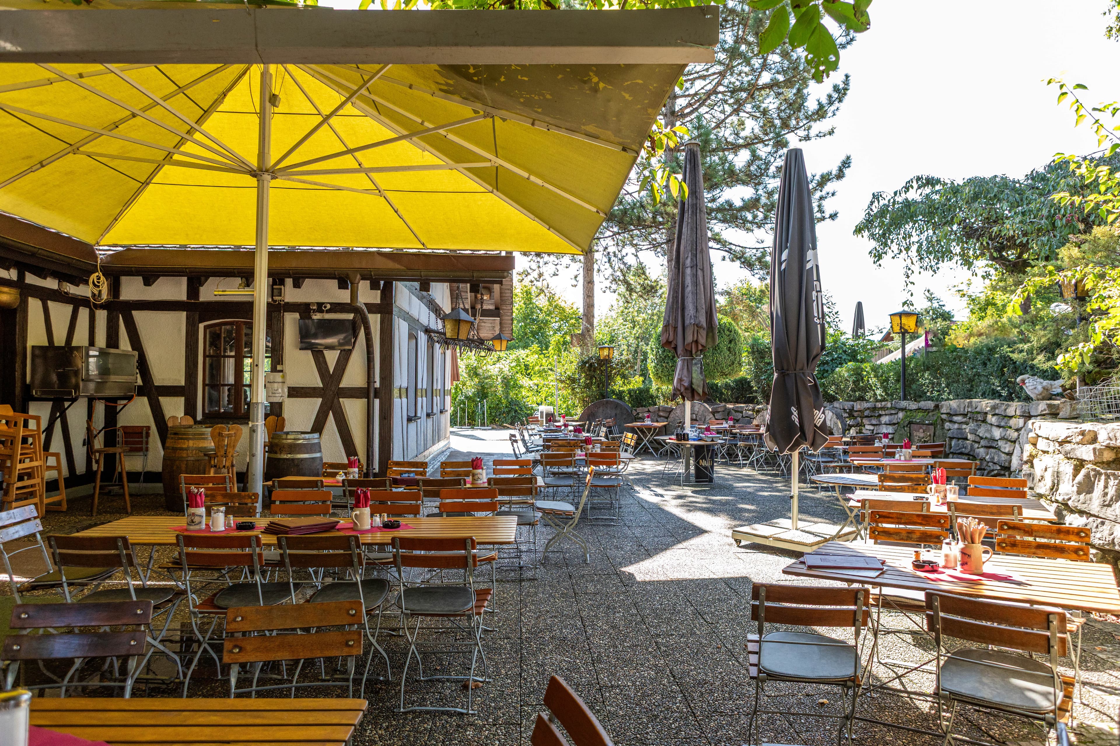 Hier ist die Gartenwirtschaft der Lochmühle Eigeltingen mit ihren Stühlen und Tischen unter Sonnenschirmen zu sehen.