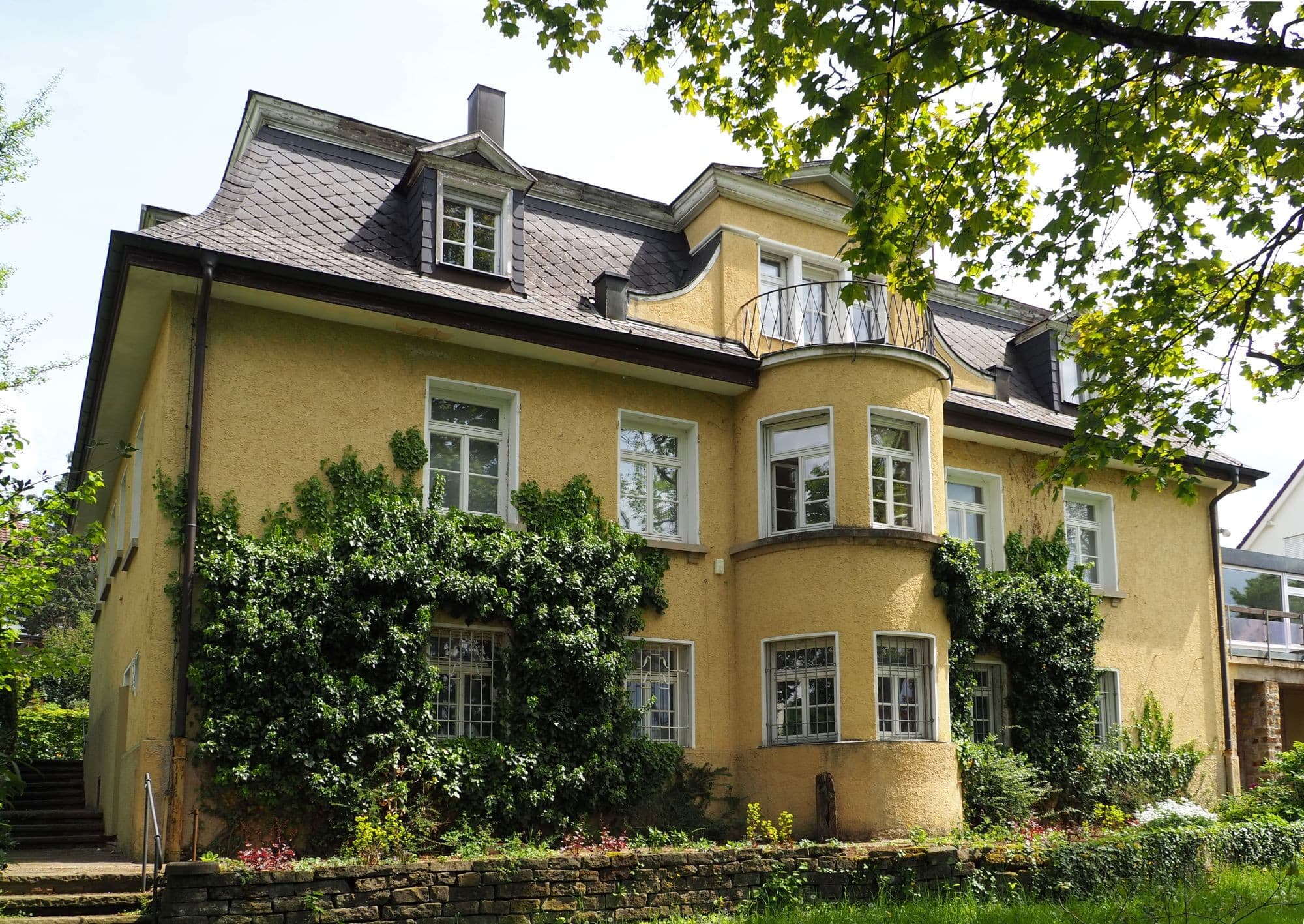 Gelbe Villa mit Efeu bewachsen und Garten im Vordergrund.