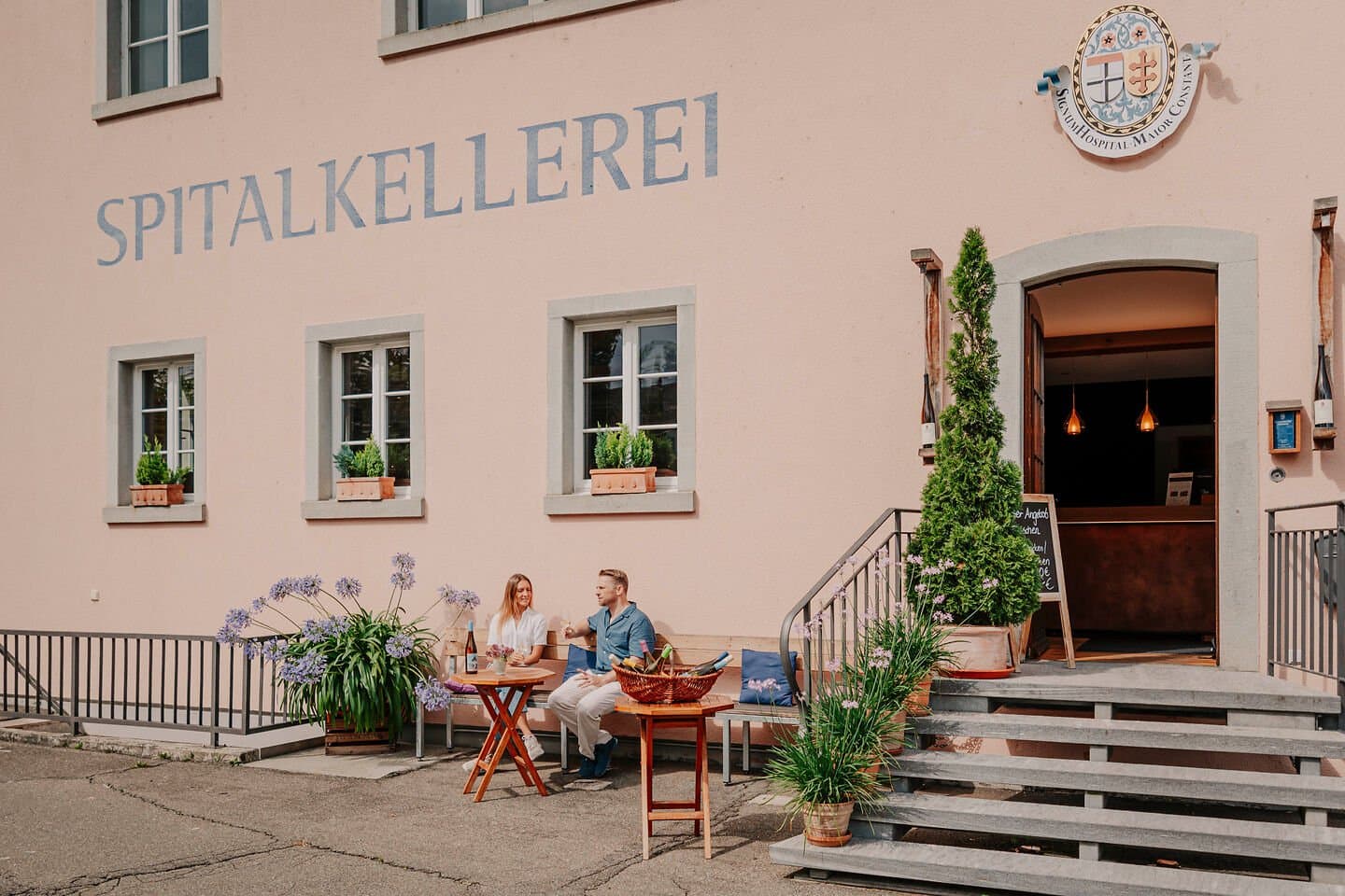 Die Spitalkellerei Konstanz von außen mit einem kleinen Tisch, an dem ein Paar mit einem Gläschen Wein sitzt