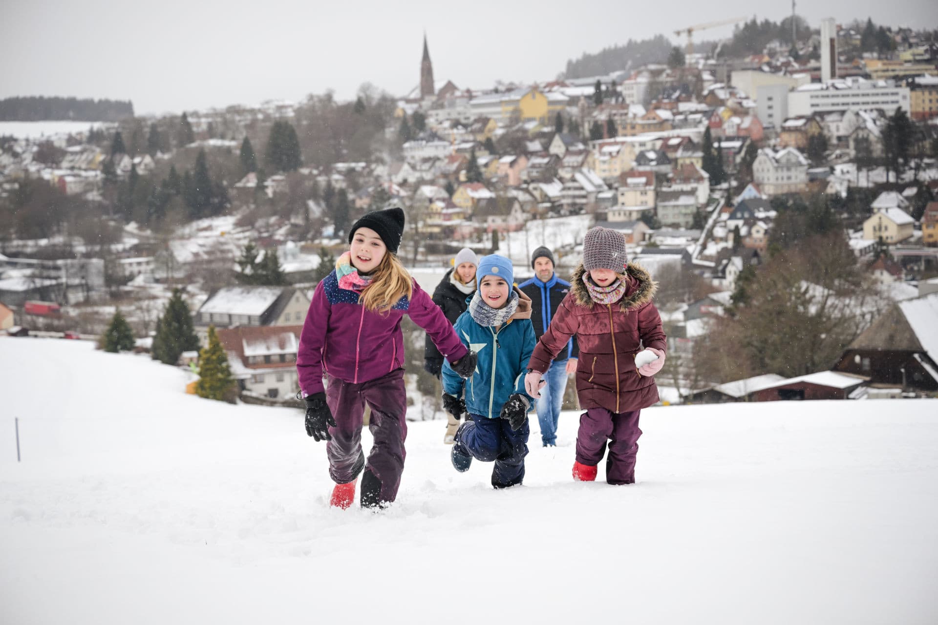 Familie beim Winterwandern, inmitten einer winterlichen Landschaft. Stadt St. Georgen im Hintergrund