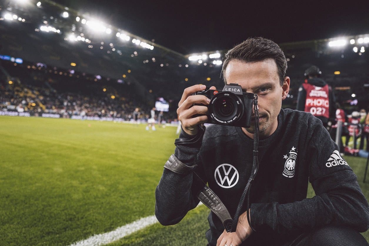 Fotograf Philipp Reinhard steht mit seiner Kamera am Fußballplatz im Stadion.