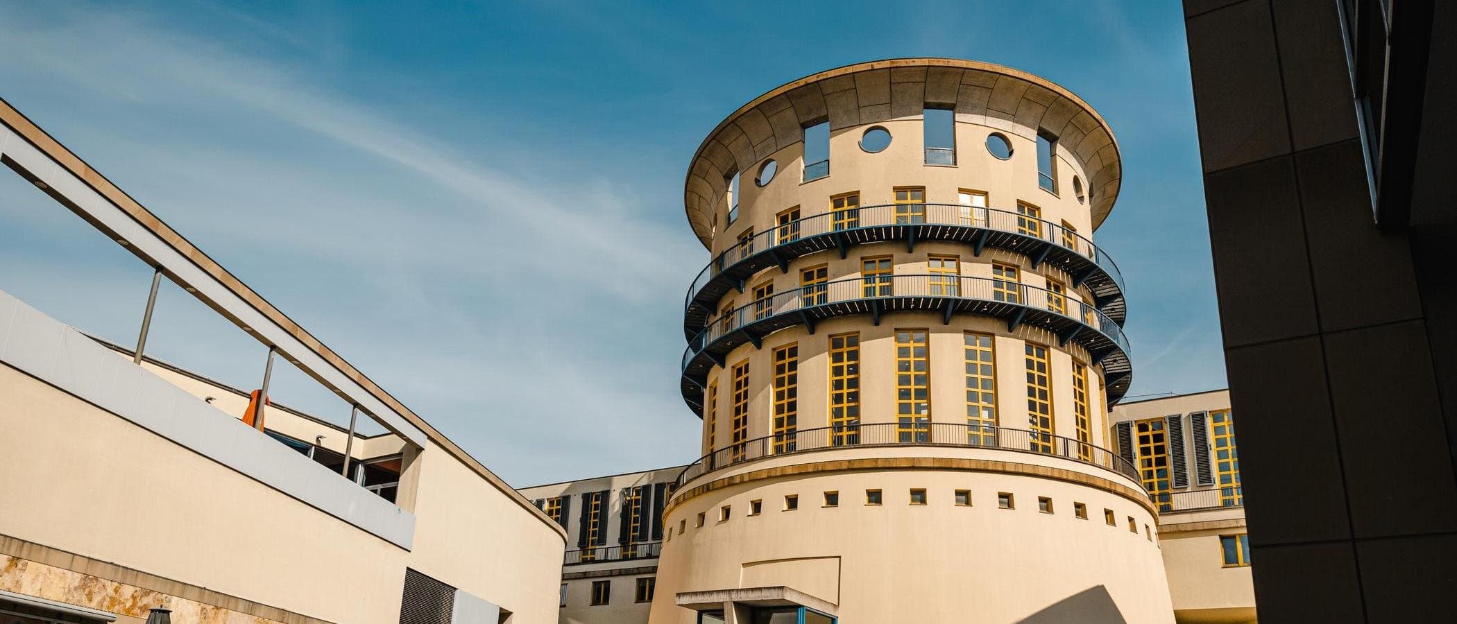 Rundes Gebäude mit modernen architektonischen Elementen und blauen Balkonen vor blauem Himmel.