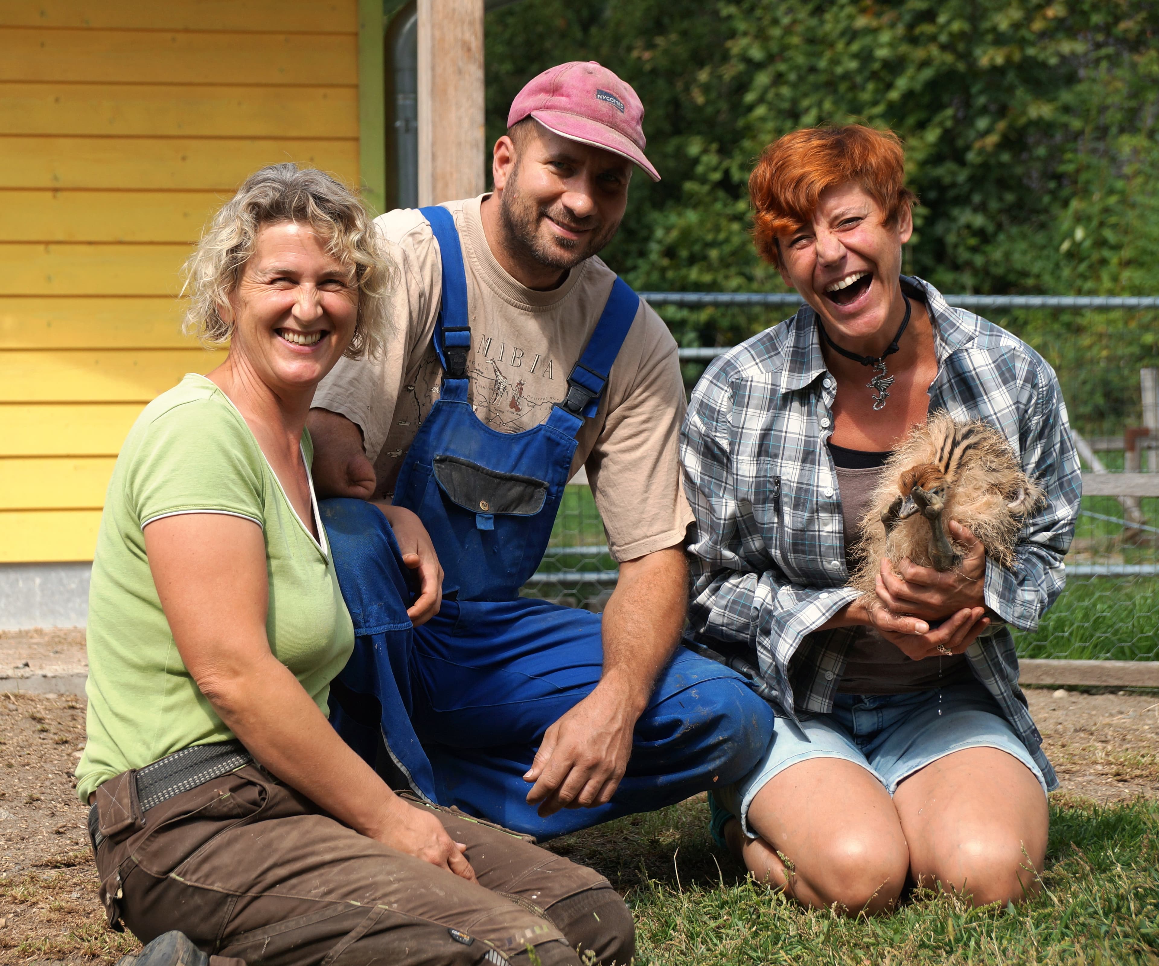 Drei Personen auf dem Boden mit einem jungen Strauß knieen auf dem Boden