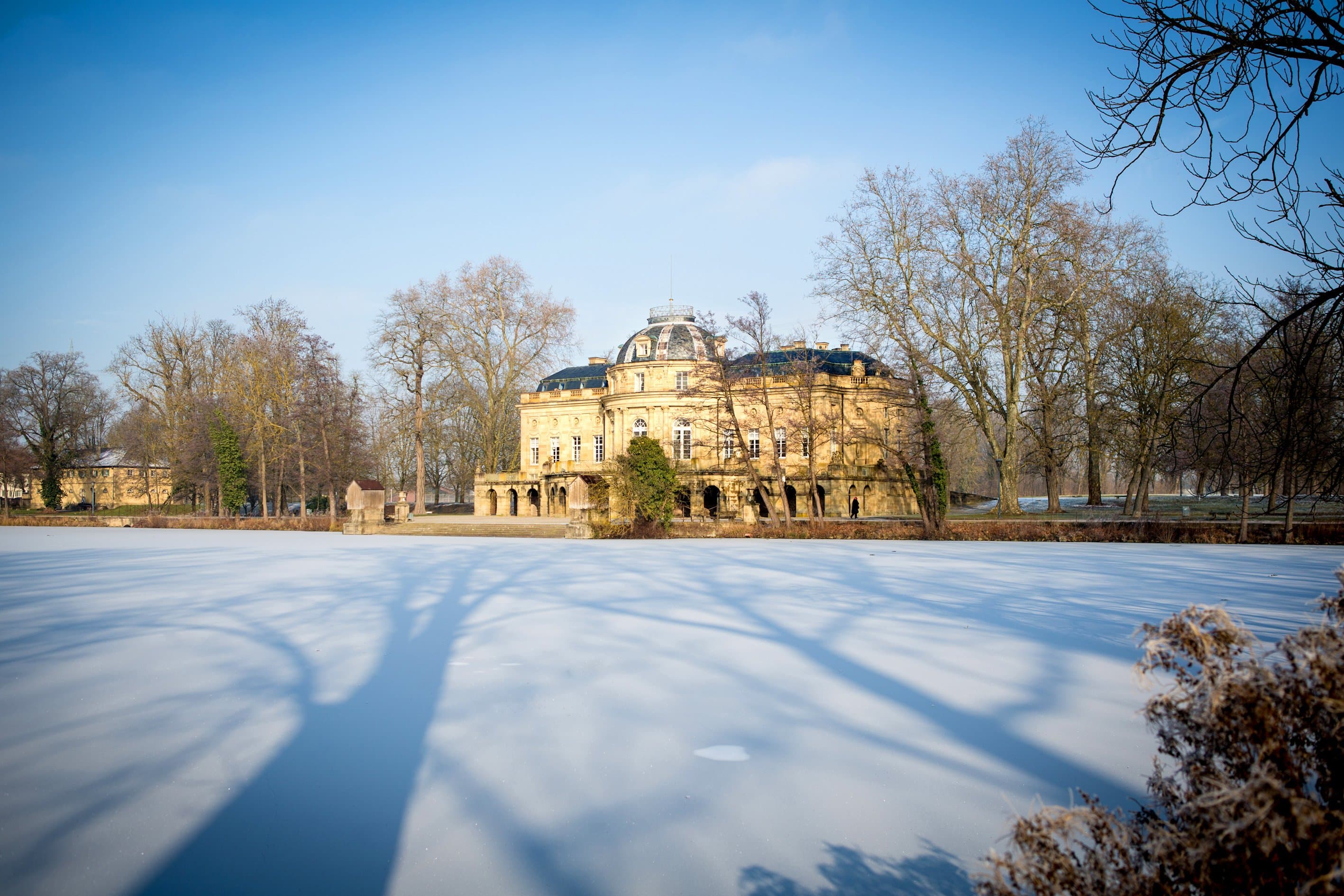 Seeschloss Monrepos im Winter mit gefrorenem See und kahlen Bäumen.