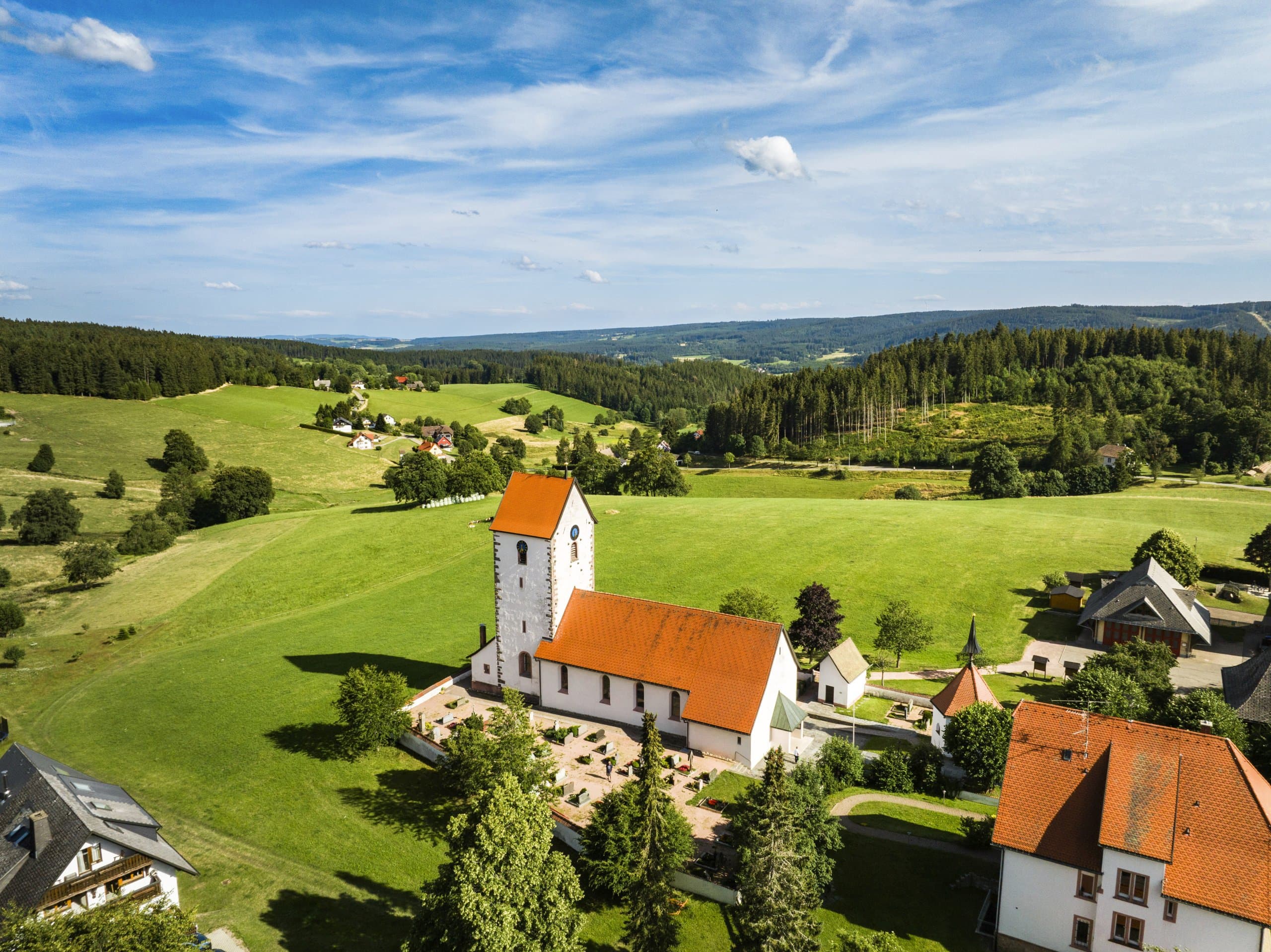 Ein Dorf mit einer Kirche auf einem grünen Hügel inmitten von Wäldern.