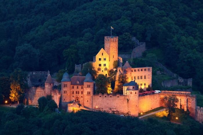 An illuminated castle on a hill surrounded by trees.