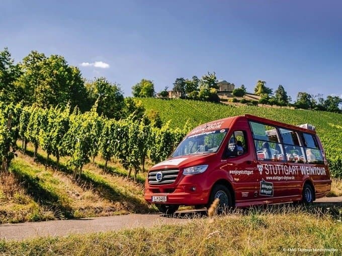 Ein roter Tourbus fährt durch Weinberge in Stuttgart bei sonnigem Wetter.