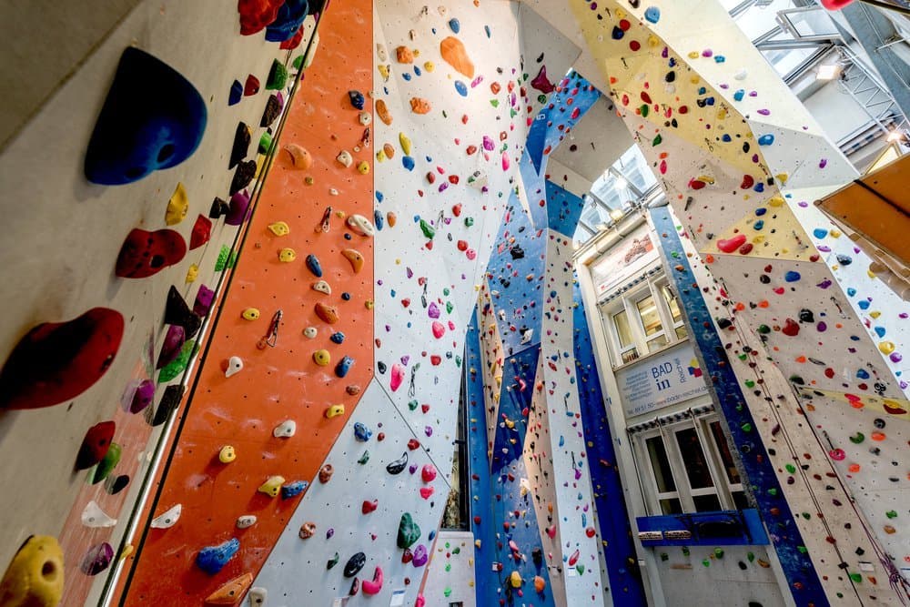 Innenansicht einer Kletterhalle mit bunten Klettergriffen an hohen Wänden.