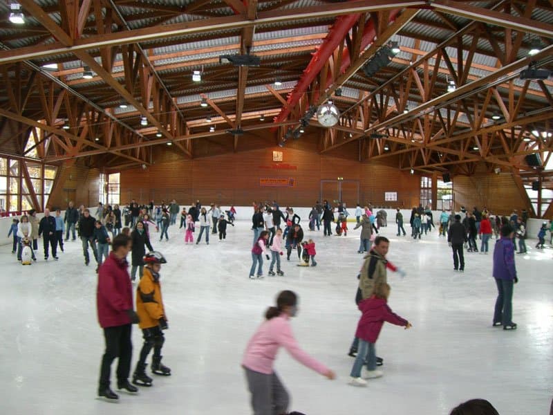 Menschen beim Schlittschuhlaufen in einer Eishalle mit Holzdach.