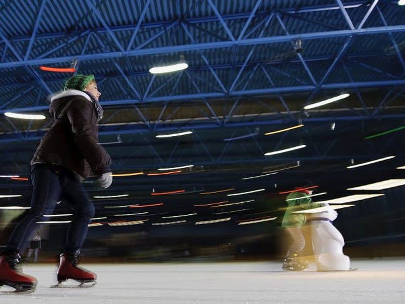 Person beim Eislaufen in einer Halle mit blauer Decke.